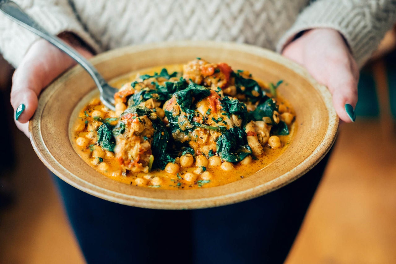 Woman holding bowl of chickpea spinach curry.