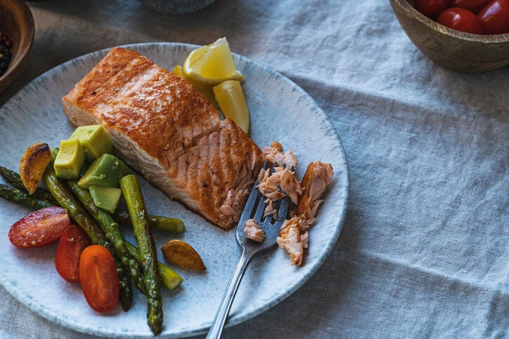 Roasted salmon fillet on a plate with asparagus spears, tomatoes, avocado and lemon wedges.