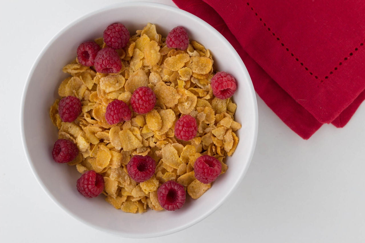 Bowl of cereal with raspberries on a white surface with a red napkin.
