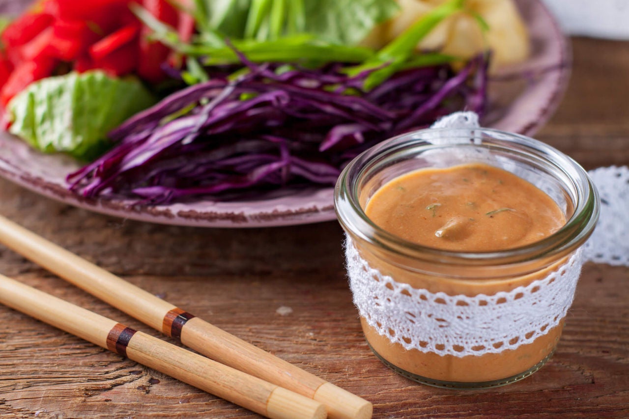 Peanut sauce in a small glass jar next to a pair of chopsticks and a plate with shredded cabbage.