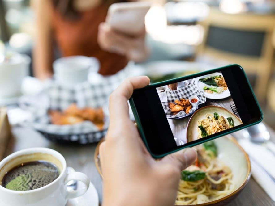 Hand holding mobile phone showing an image of food on a table.