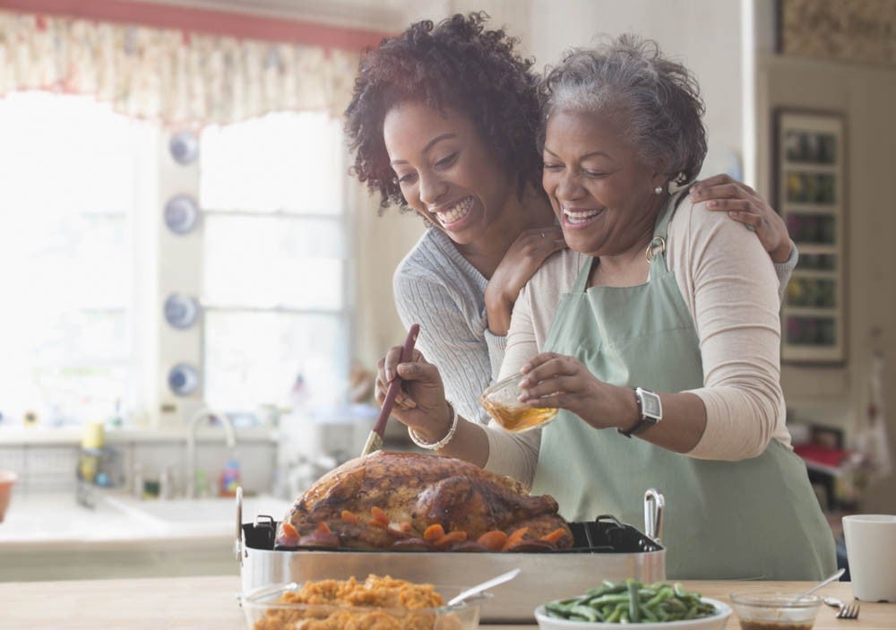 Dos mujeres en la cocina sonriendo mientrsa preparan un pavo asado juntas