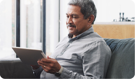  A man sits on his couch, holding a tablet.