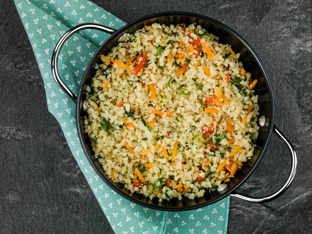 Olla con arroz pilaf de vegetales llena de verduras coloridas, sobre una servilleta azul con estampado y fondo oscuro
