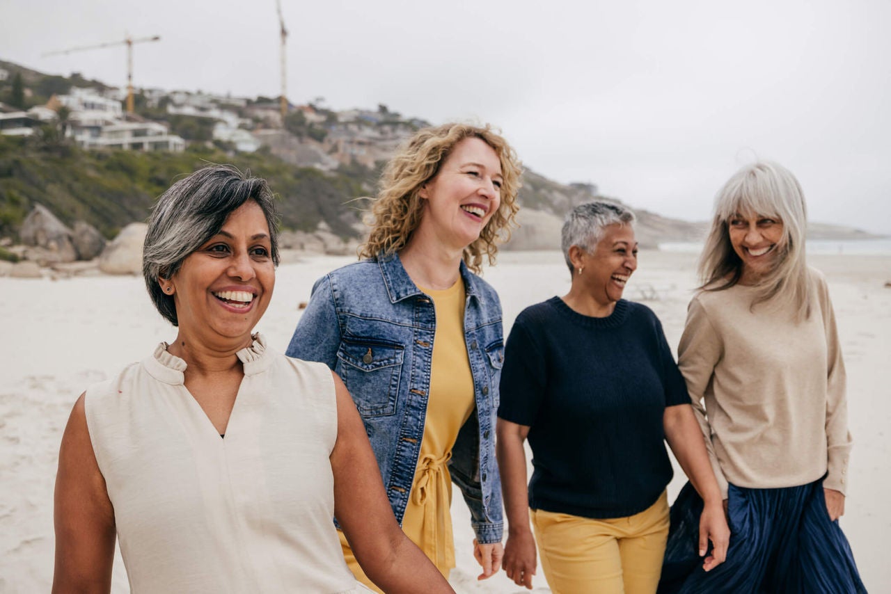 Group of middle aged women walking on a beach during daytime, smiling.