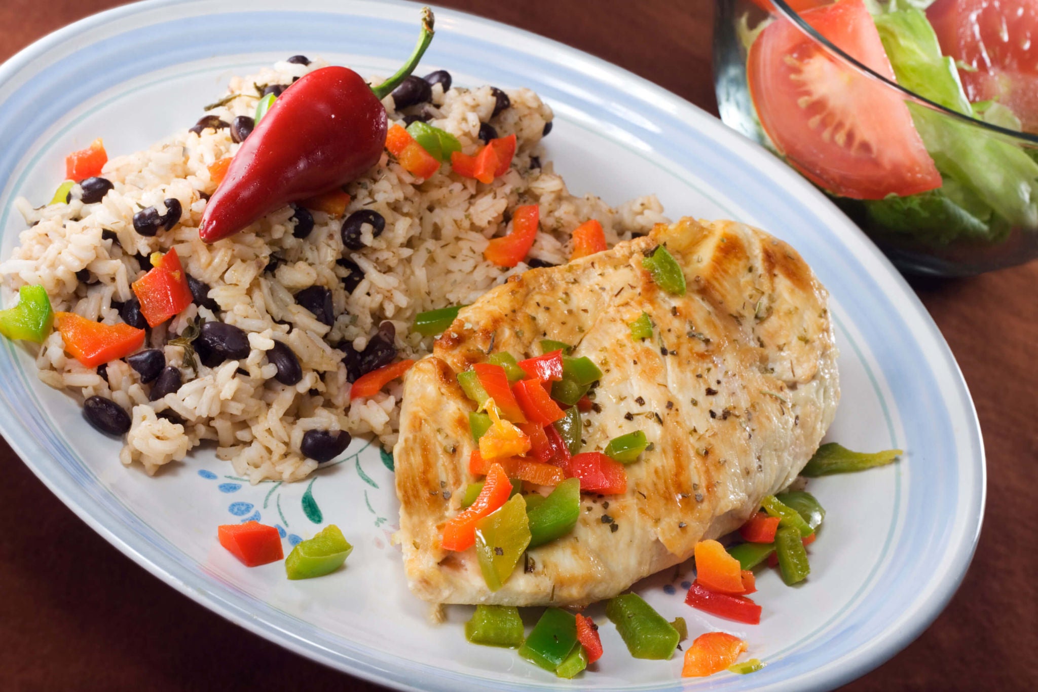 Chicken breast with bell peppers, rice and beans, and a whole chili.