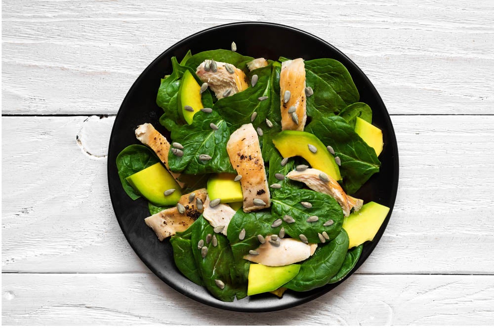 Chicken salad with avocado, spinach and tomatoes cherry in black plate. healthy food. top view