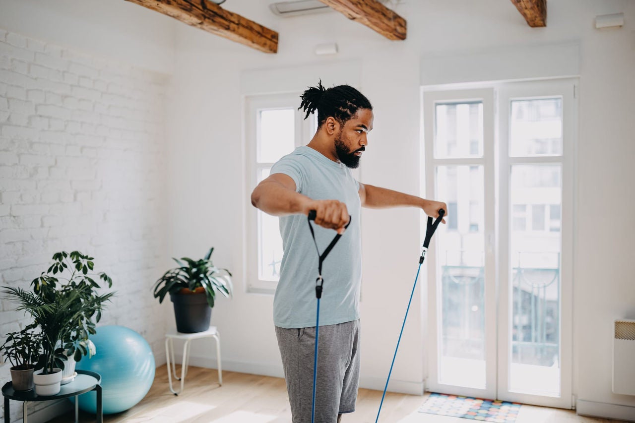 Man exercising with resistance bands in a bright home gym.