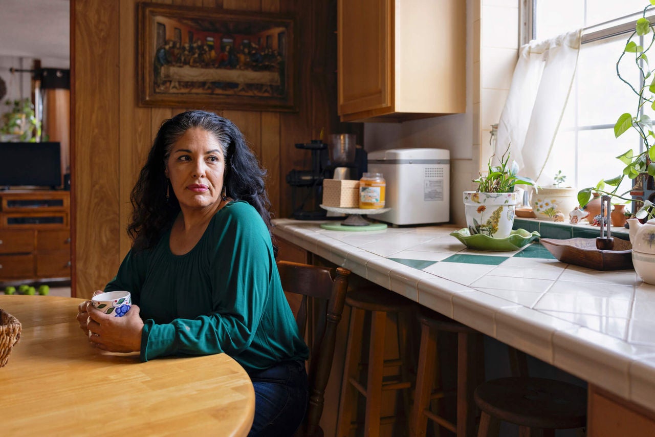 Woman sitting contemplatively at a kitchen table with a mug. 