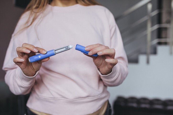Woman standing and holding an injection pen with the cap in the other hand. 