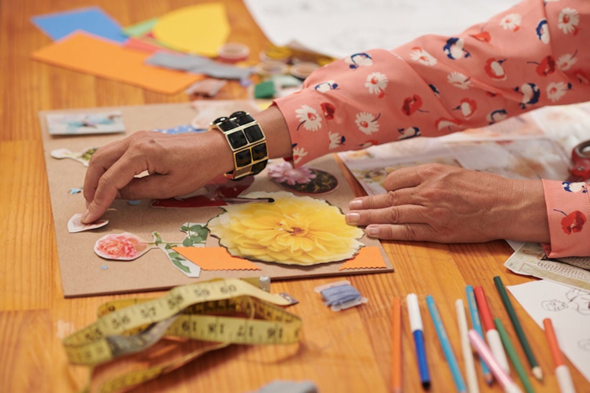 Woman's hand gluing images cut from a magazine onto a cardboard background