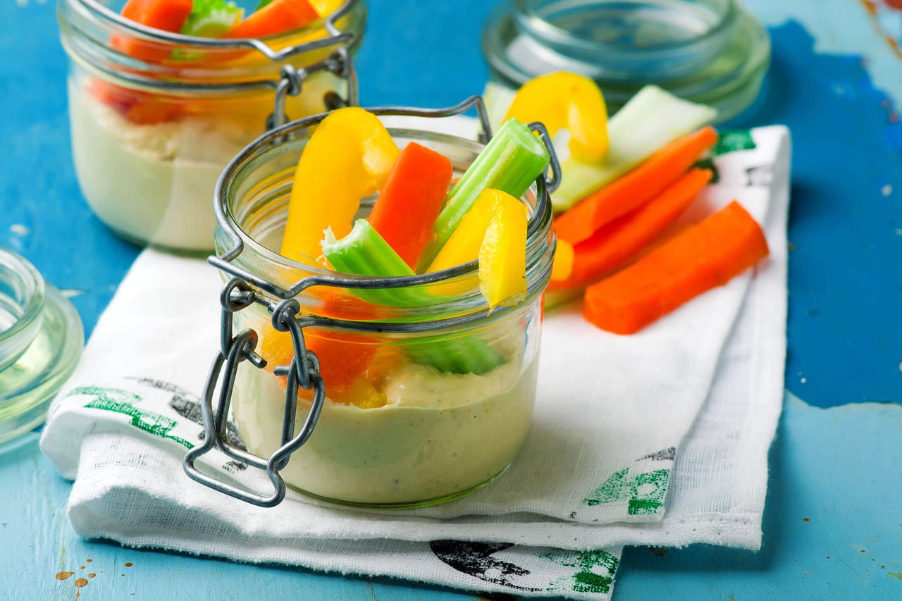 Jars with hummus at the bottom, sliced vegetables on top. 