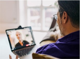 A man speaks virtually with another man on a laptop.