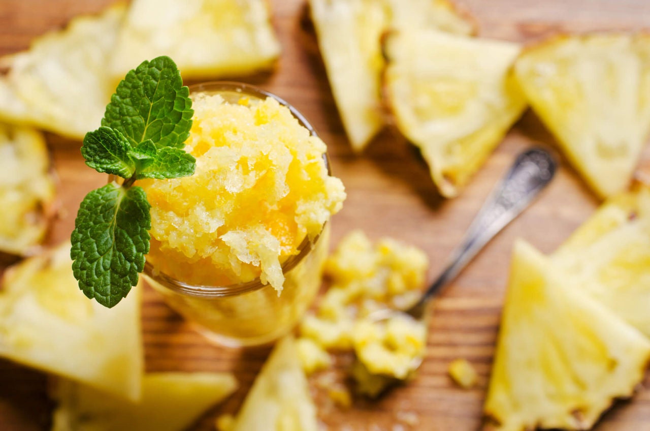 Pineapple shaved ice topped with mint, with pineapple slices and a spoon in the background.