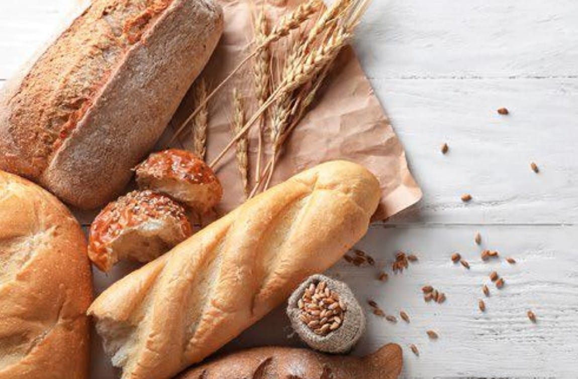 Assortment of bread with wheat stalks on brown paper on a white table