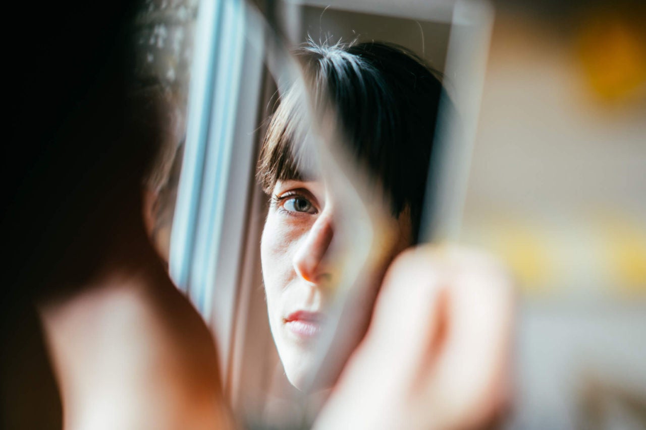 Woman staring contemplatively at her reflection in the mirror.