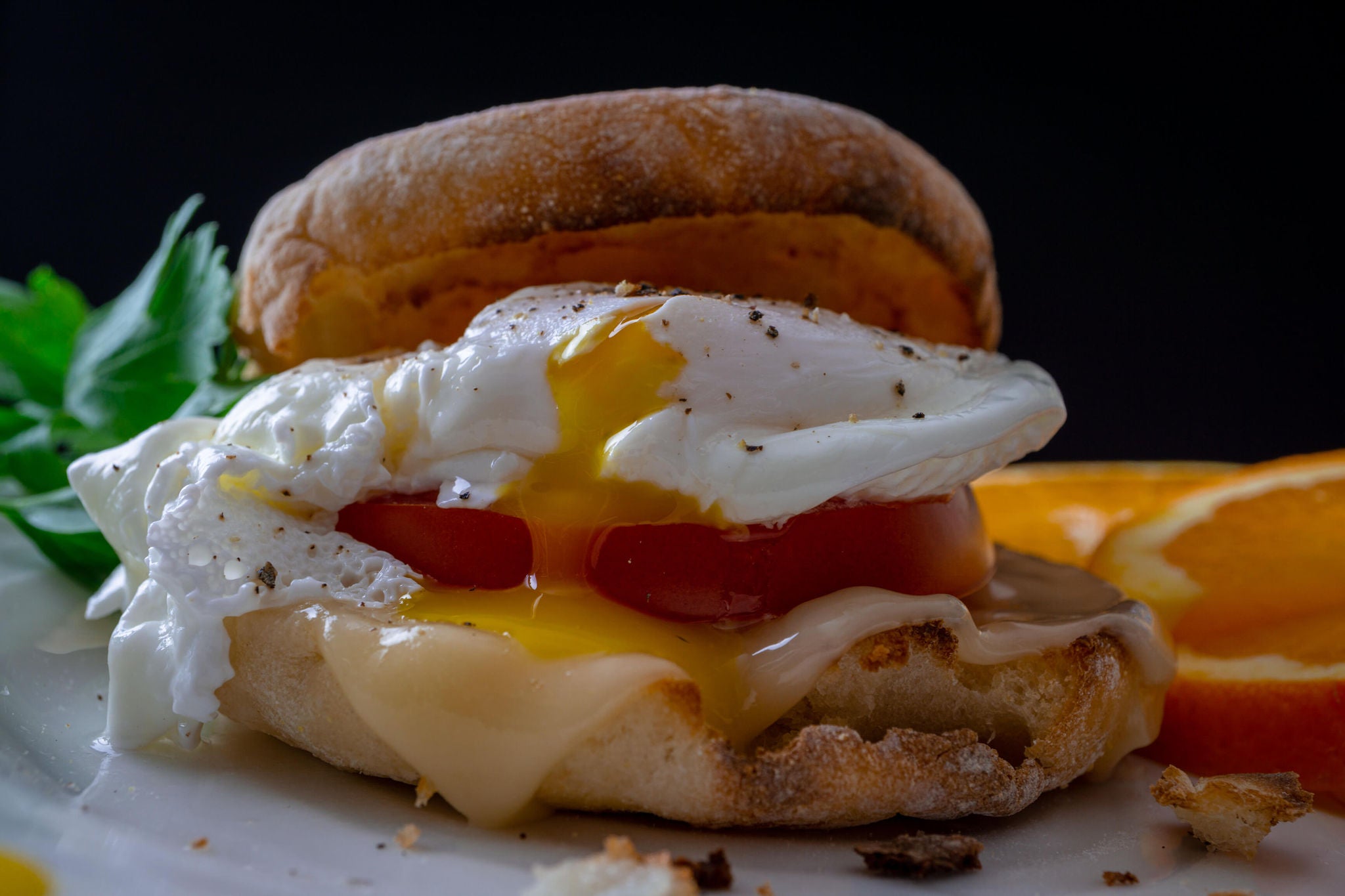 Breakfast sandwich on an english muffin with an egg, tomato and cheese.