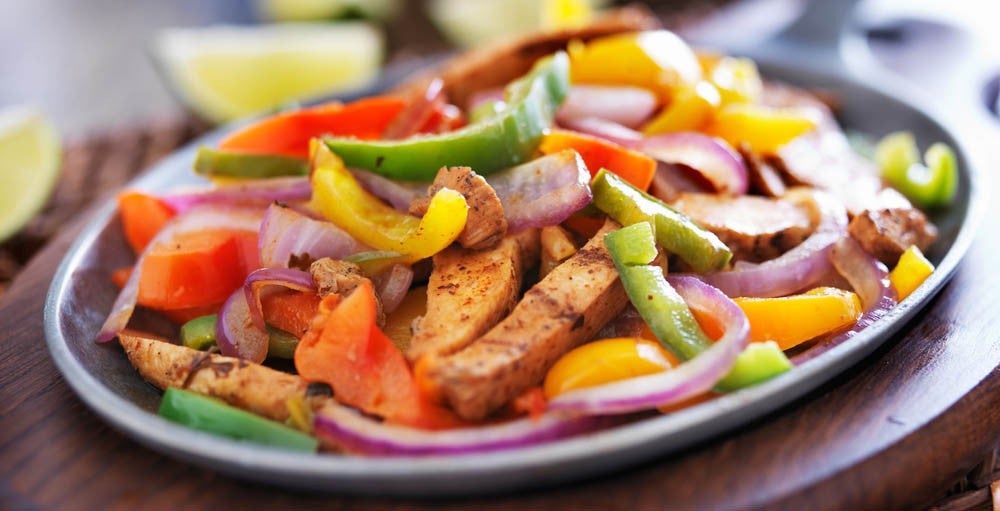 Plato de fajitas con pollo, pimientos de colores y cebolla morada.