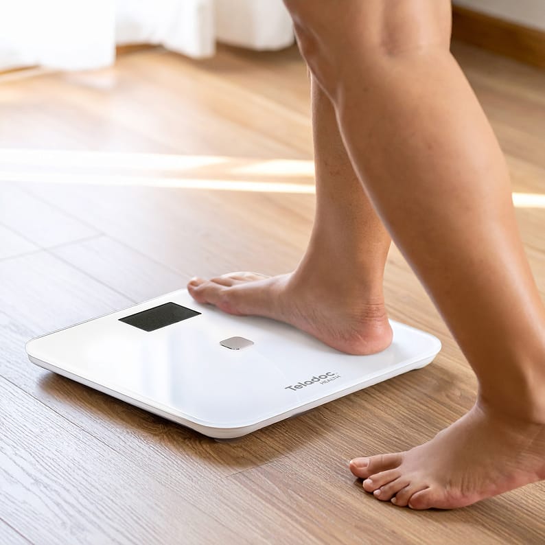 Close-up of bare feet standing on a Teladoc Health smart scale.