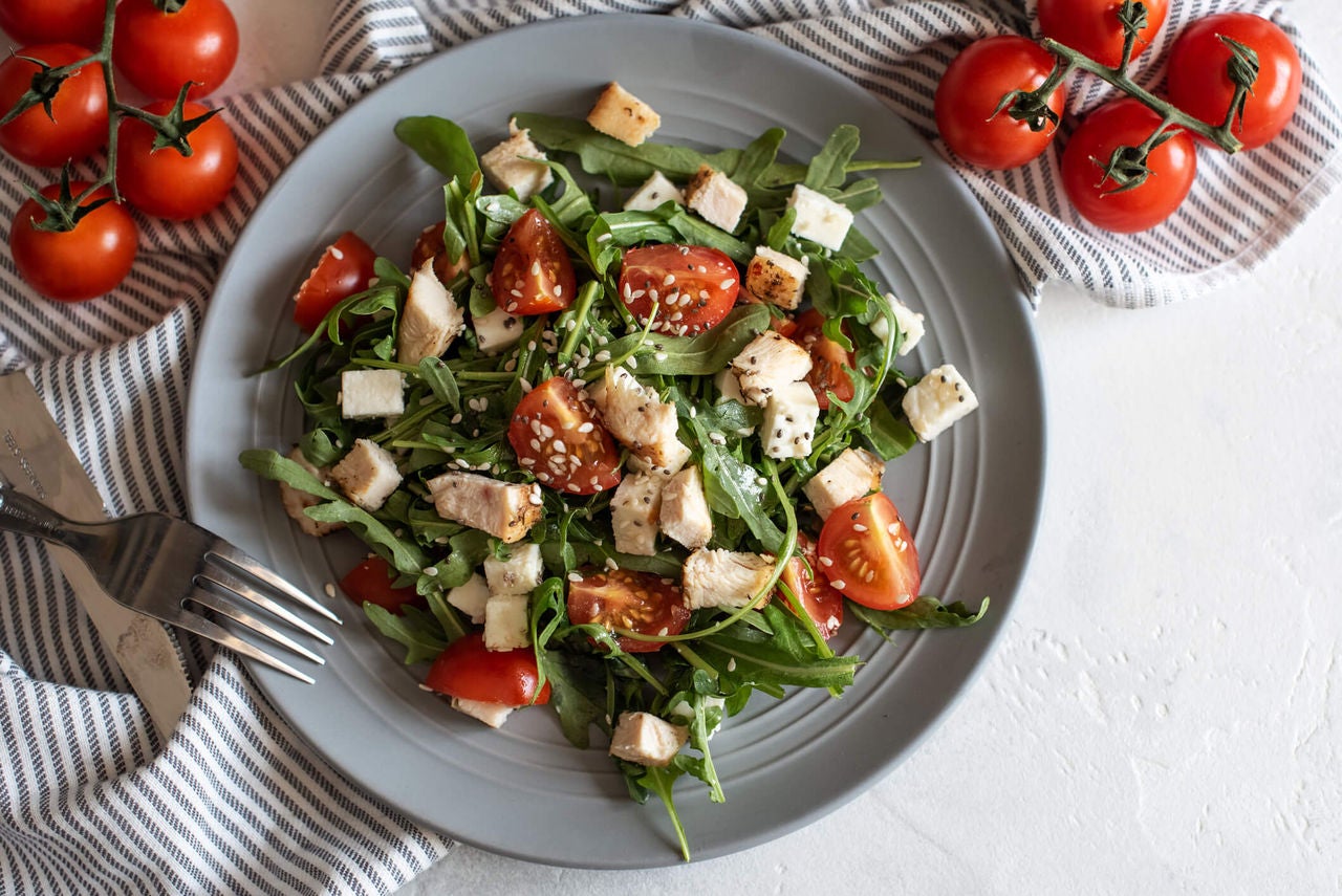 Salad with grilled chicken pieces, quartered tomatoes and feta cubes.