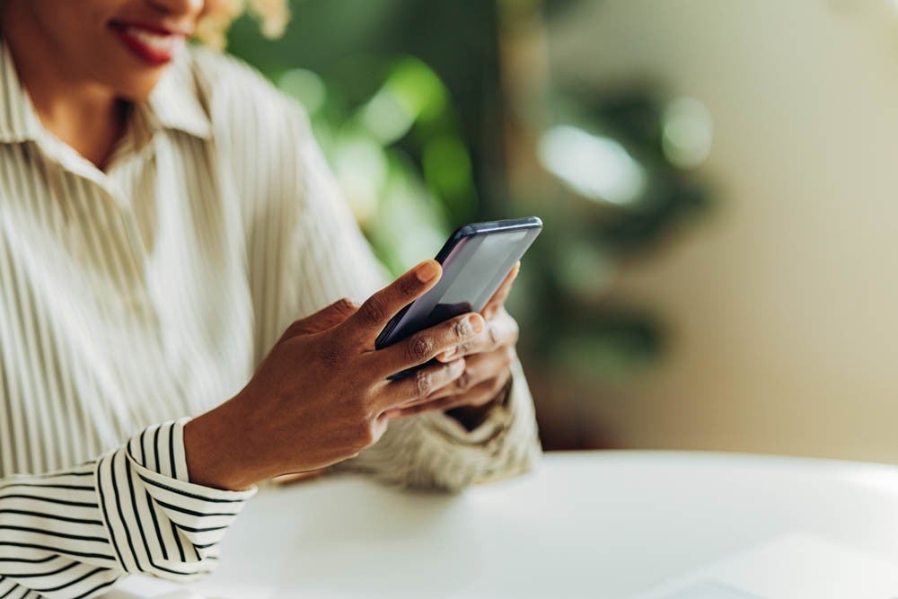 An anonymous African American woman typing text message on her smartphone while sitting at office desk.