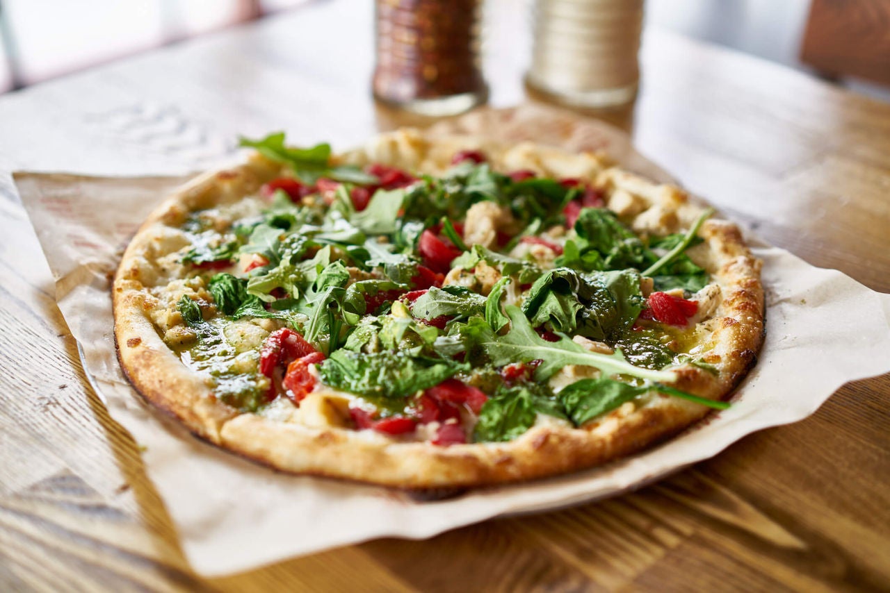 Pizza with arugula, tomatoes, chicken and pesto.