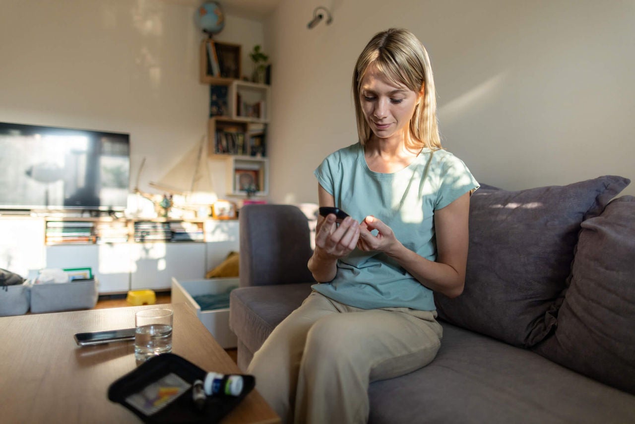 Woman sitting on couch checking blood sugar