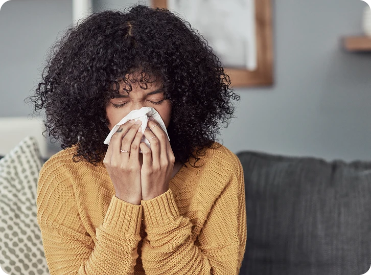  Woman sitting indoors holding a tissue while experiencing allergy or sinus symptoms.