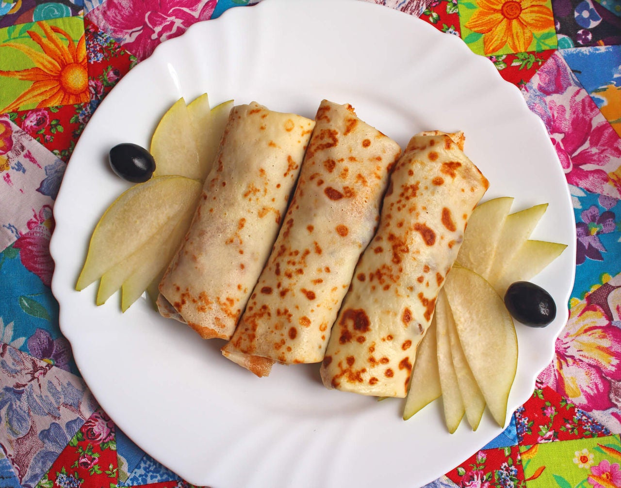 3 rolled quesadillas with slices of pear and two grapes on a colorful background.