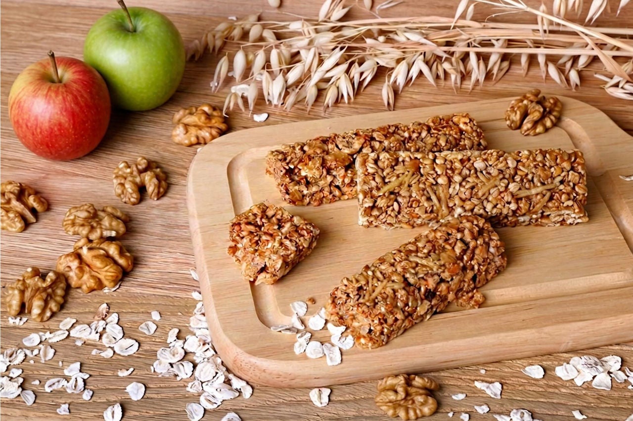 Cutting board with baked oatmeal bars surrounded by walnuts, oats and apples.