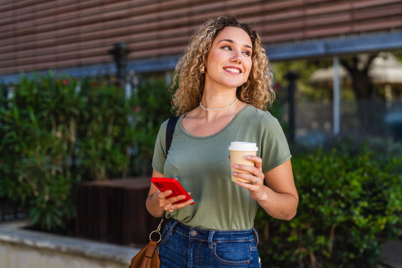 Woman standing outside smiling while holding a to-go coffee cup.
