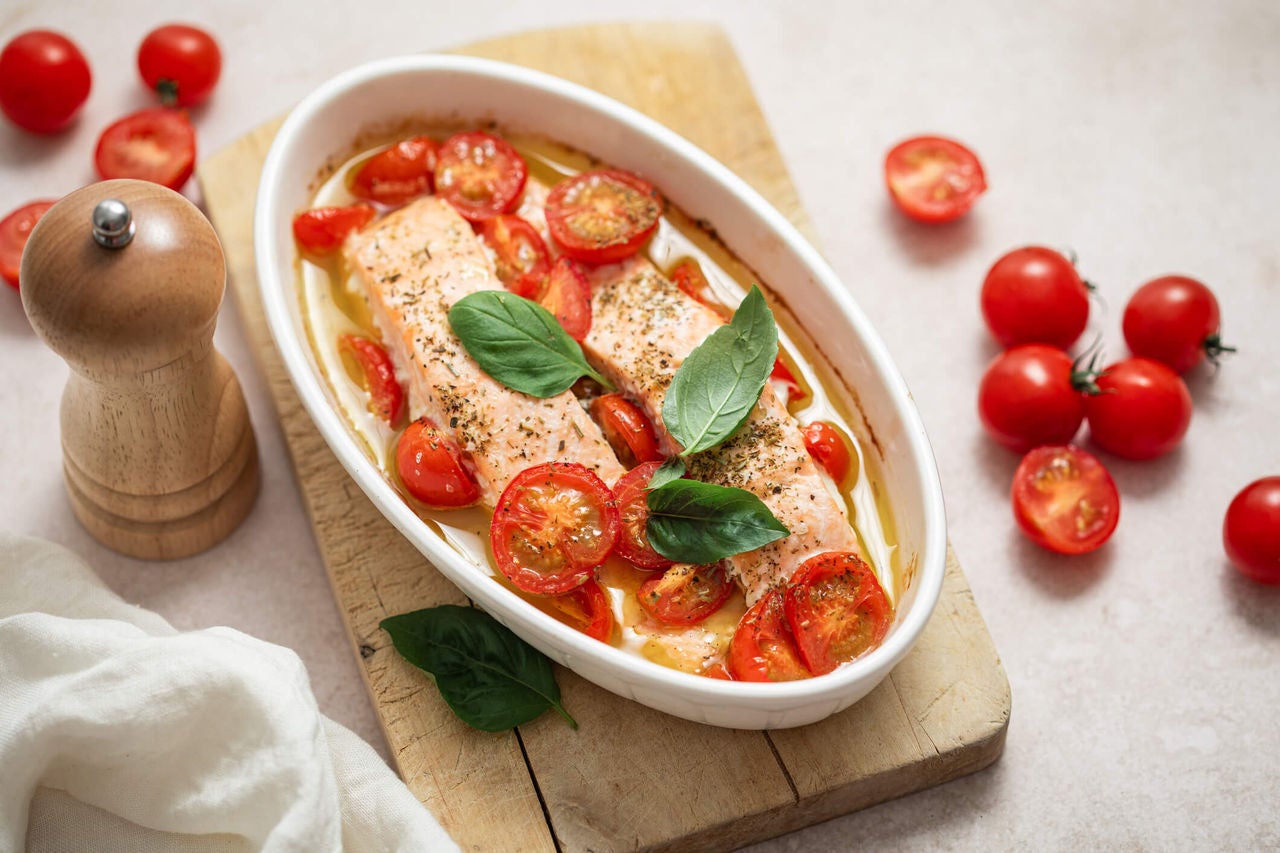 Baking dish with salmon fillets seasoned with pesto and cherry tomatoes.