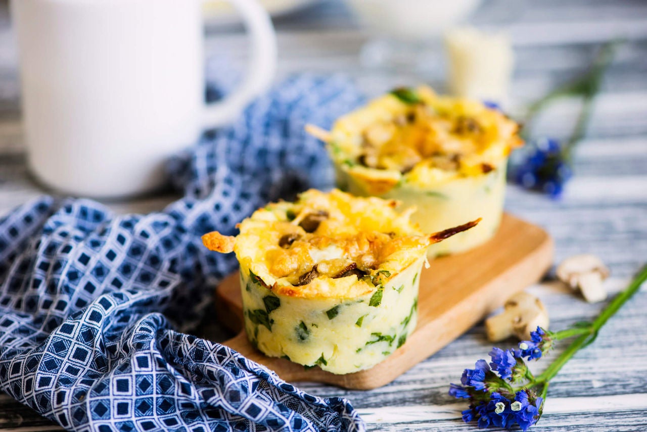 Egg cups with asparagus, mushroom and greens with a mug, tablecloth and flowers surrounding.