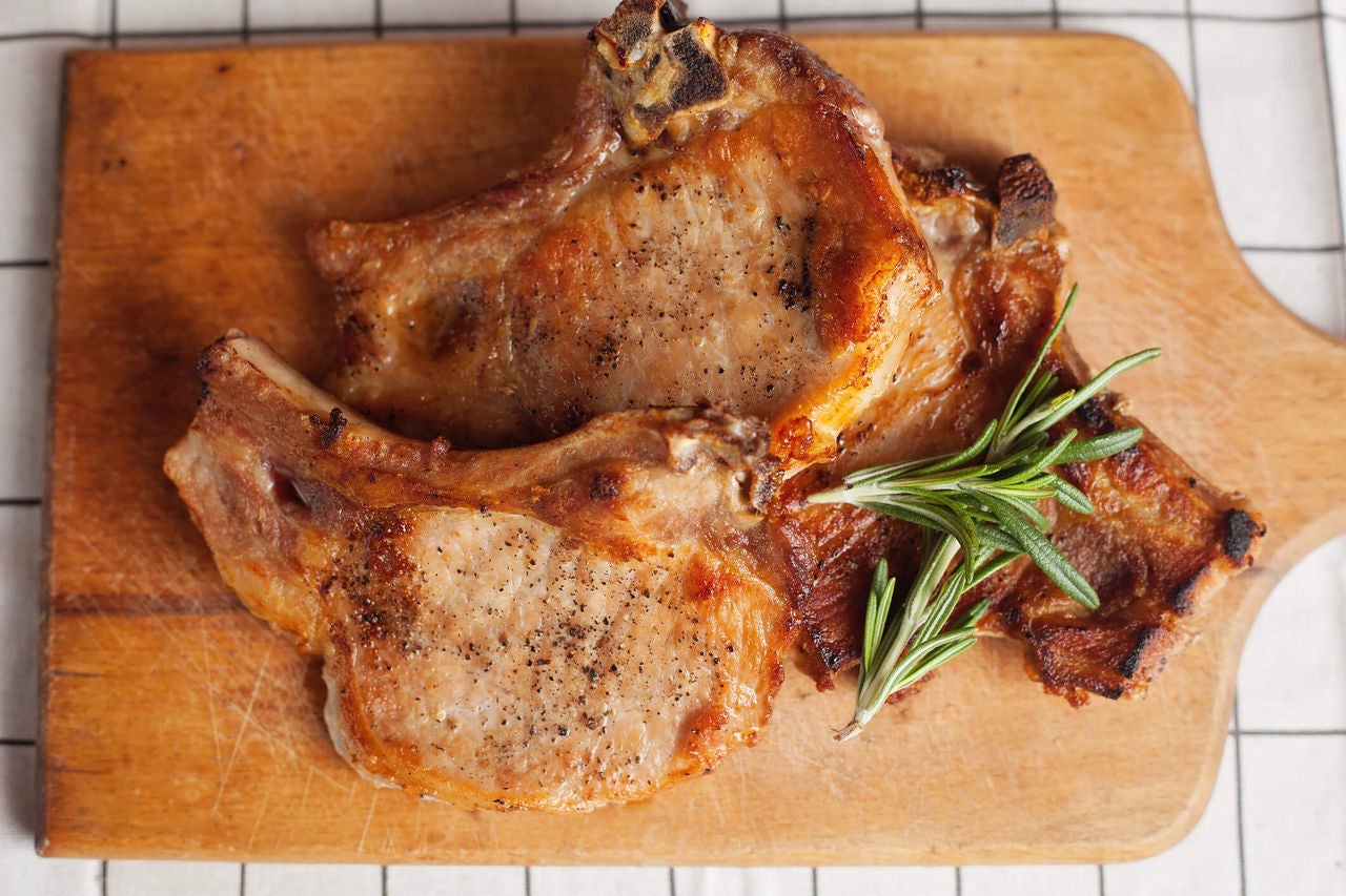 Seasoned pork chops on a wooden board with rosemary sprigs.