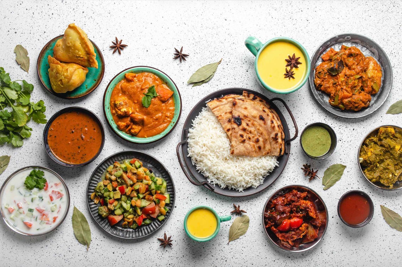 Overhead view of various South Asian cuisines on a table surface, garnished with leaves and spices.