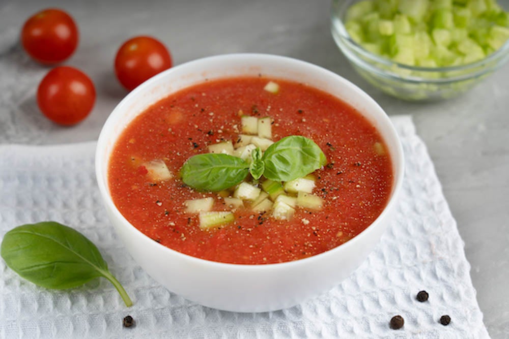 Gazpacho de tomate y frijoles blancos en tazón blanco decorado con albahaca fresca