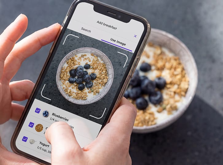 Hands holding a mobile phone taking a picture of a bowl of food
