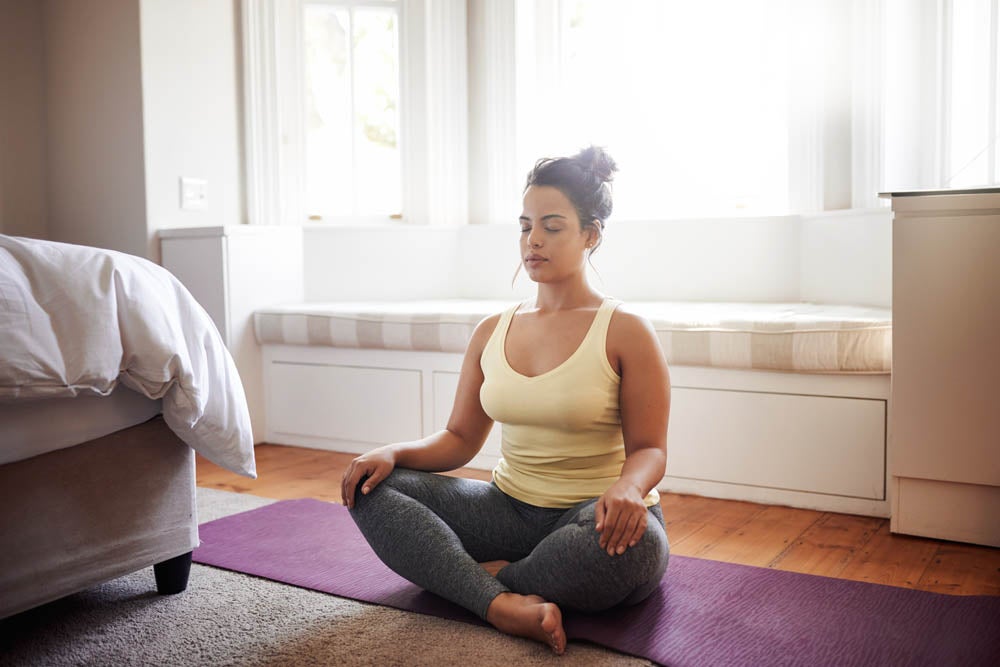 Fotografía de una mujer joven practicando yoga en casa.