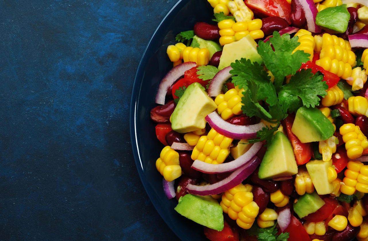 Bowl of beans, corn, avocado and onions on a dark blue background.