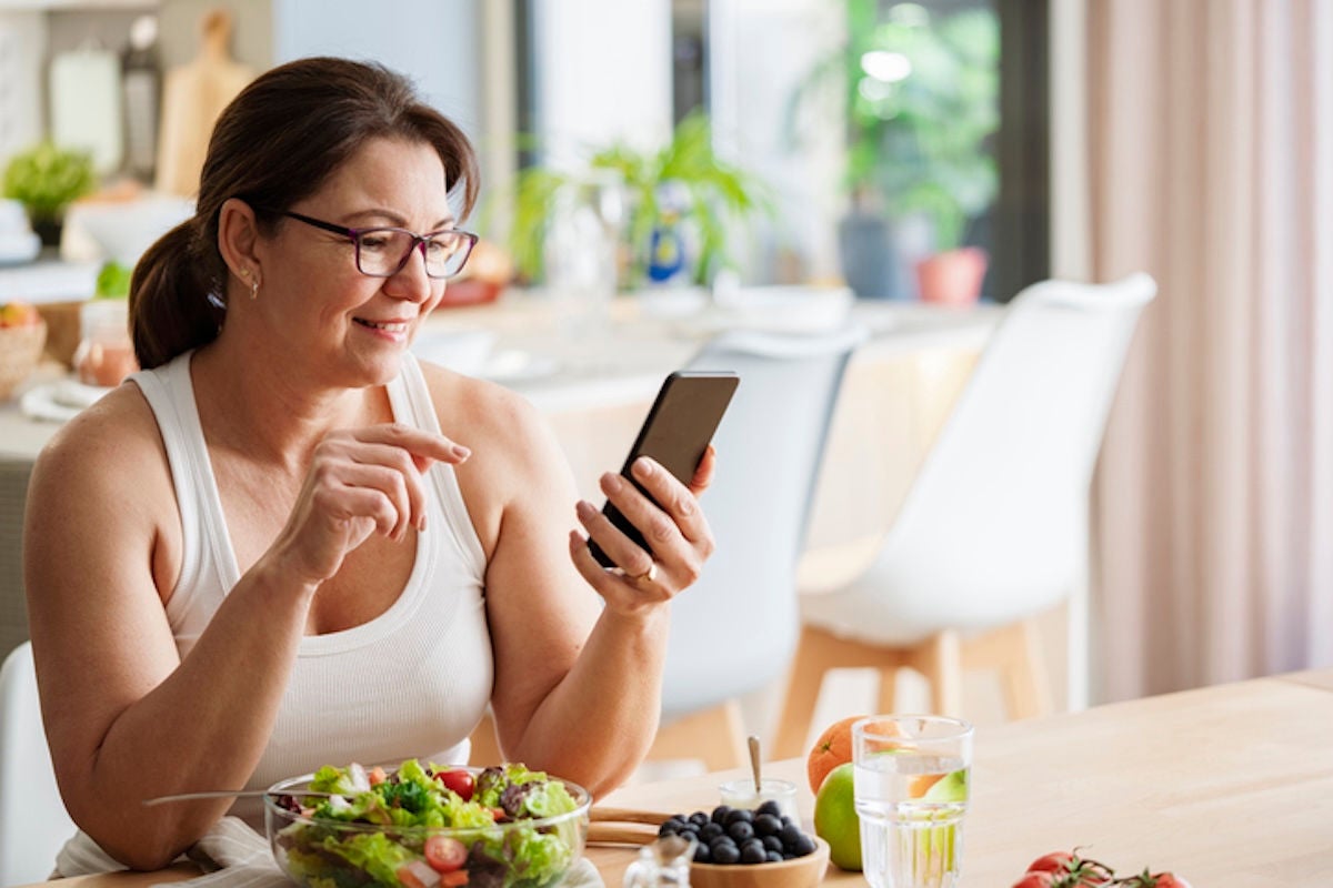woman eating a salad, smiling and looking at her phone