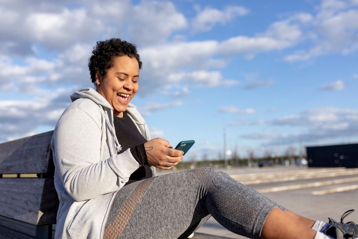  Una mujer sentada en un banco mira su teléfono y sonríe