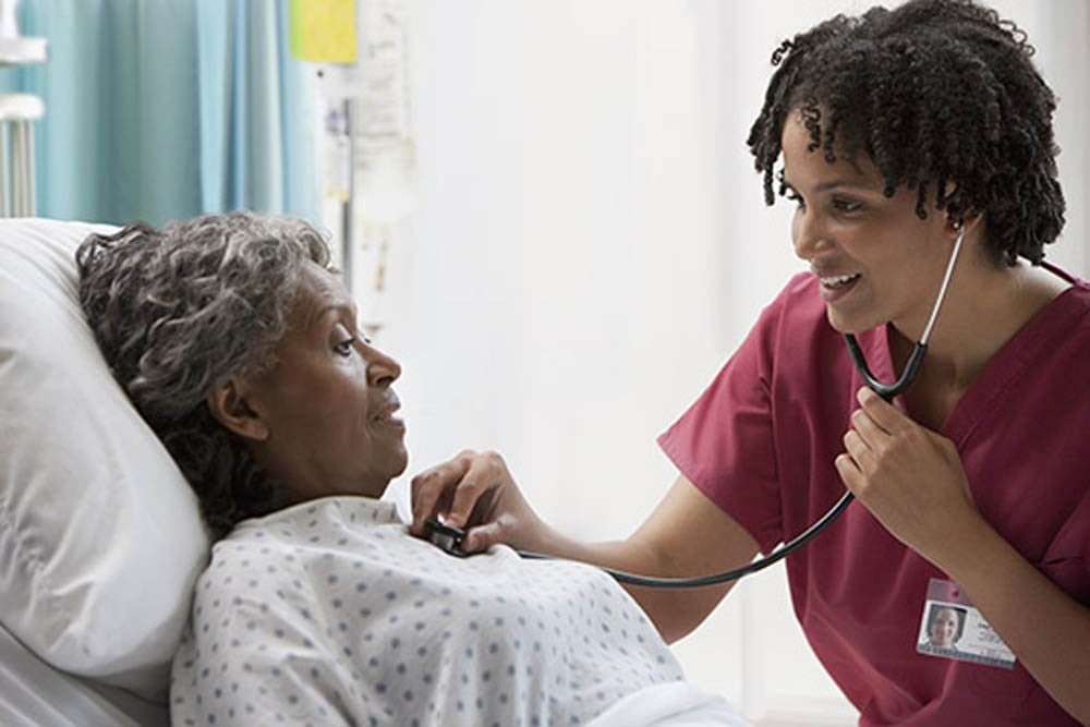 Nurse using a stethoscope to check a patient's heartbeat in a hospital bed.