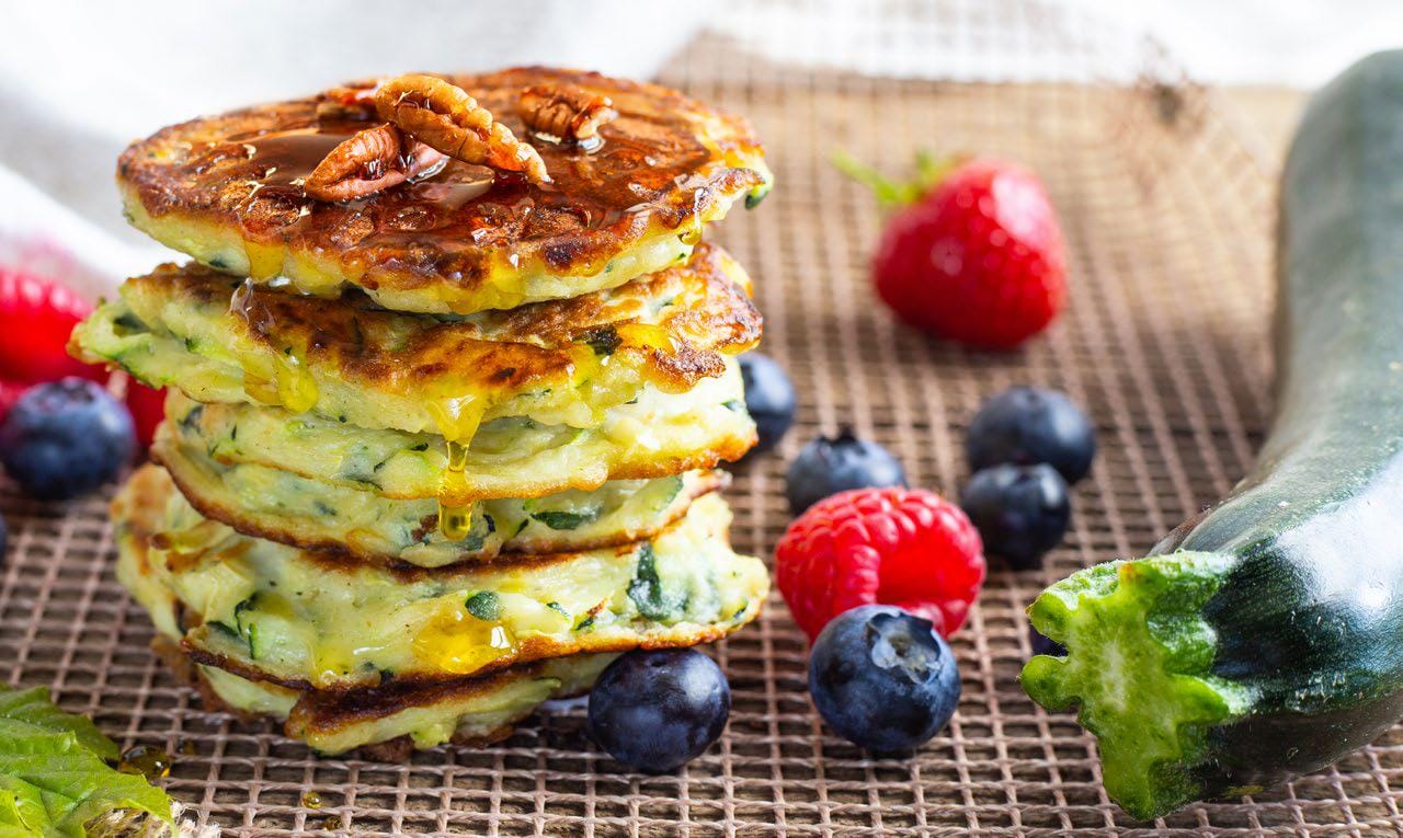 Zucchini pancakes in a stack with blueberries, raspberries, and a zucchini