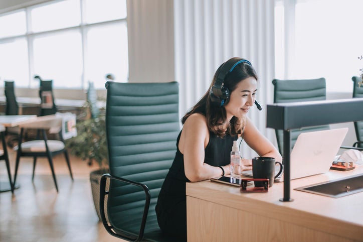 Smiling woman wearing a headset and using a laptop during an online meeting in a modern office.