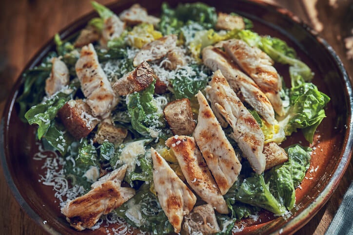 Bowl of Caesar salad with grilled chicken strips on top. 