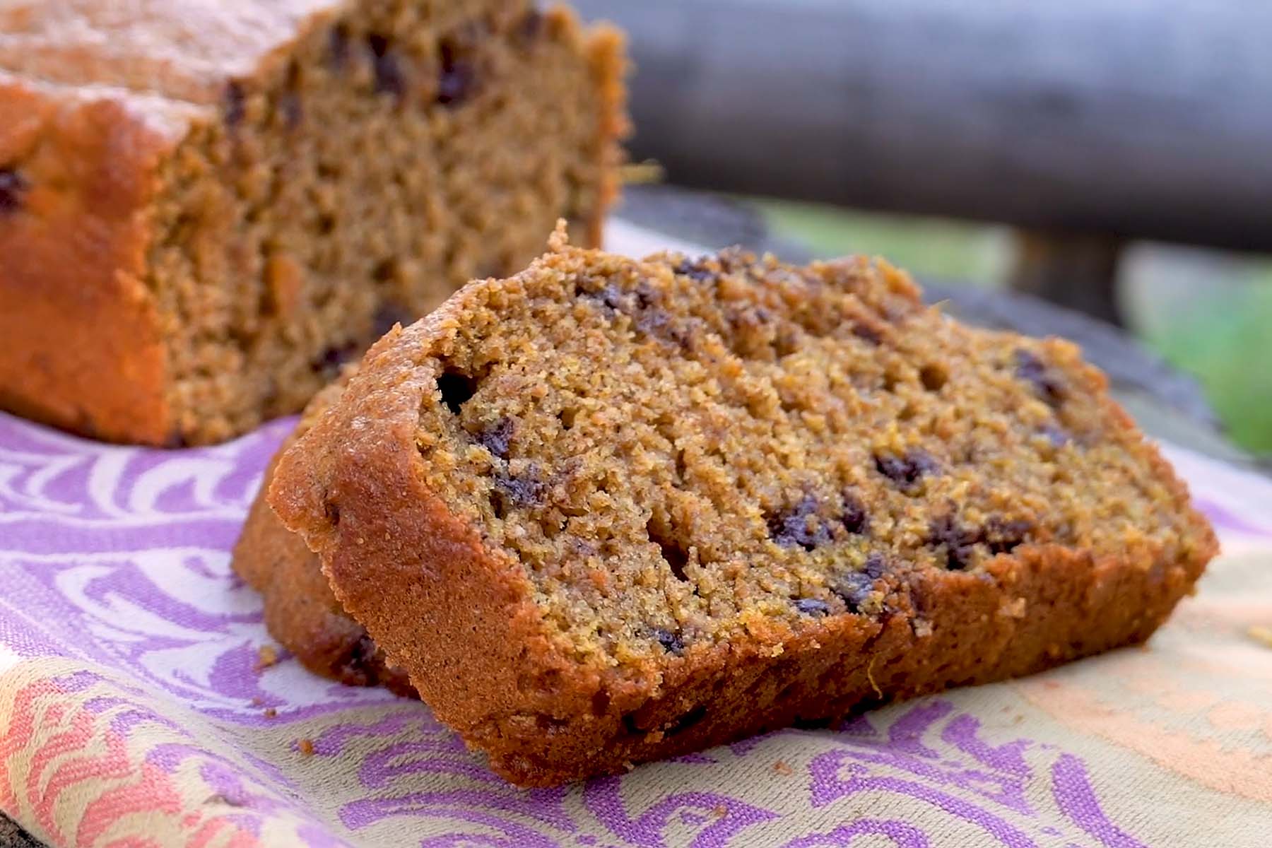 Sliced loaf of pumpkin bread with chocolate chips on a patterned cloth