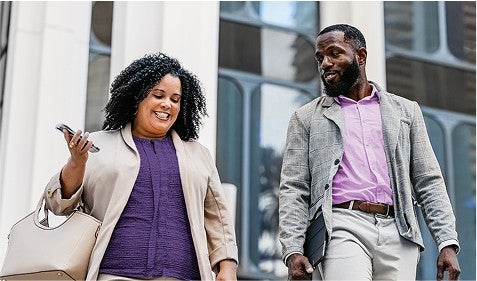 Two people in business casual clothing walk outside a building.