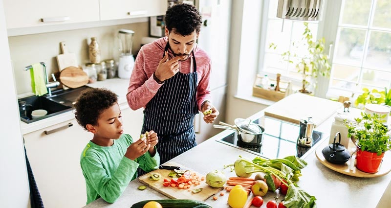 Dad and son chopping vegetables in kitchen. 