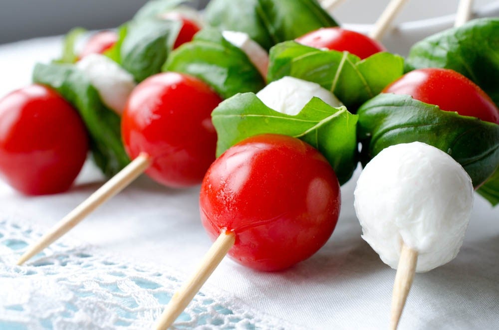 Un primer plano de brochetas con tomates cherry, hojas de albahaca fresca y bolitas de mozzarella, dispuestas ordenadamente sobre una superficie de color claro