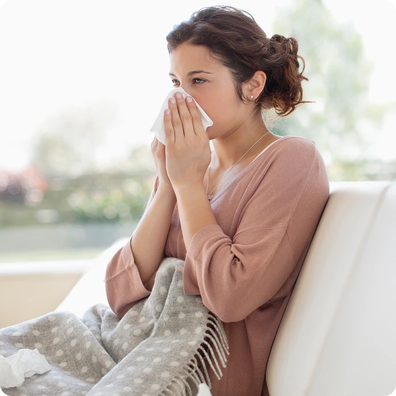 Woman sneezing into a tissue while sitting indoors during allergy season. 